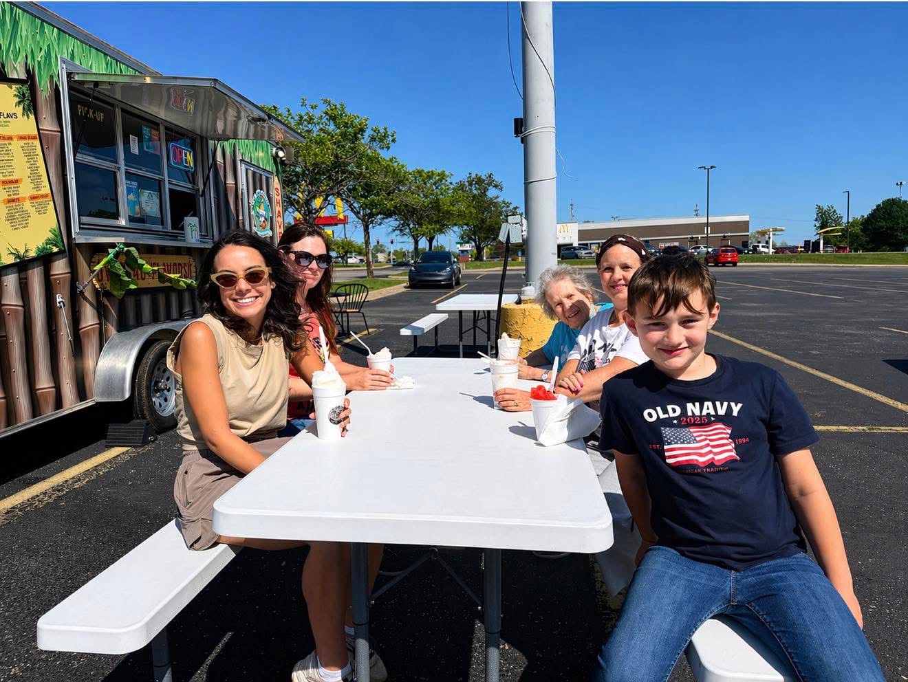 Family enjoying shaved ice at a picnic table next to the truck