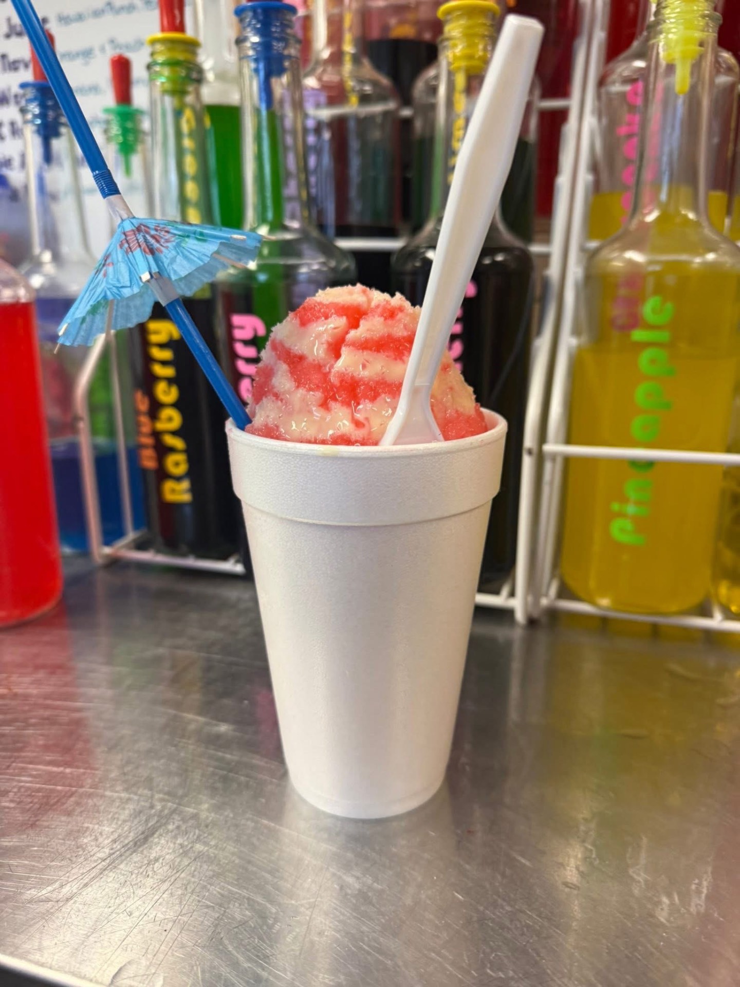 Strawberry shaved ice with colorful syrup bottles in the back